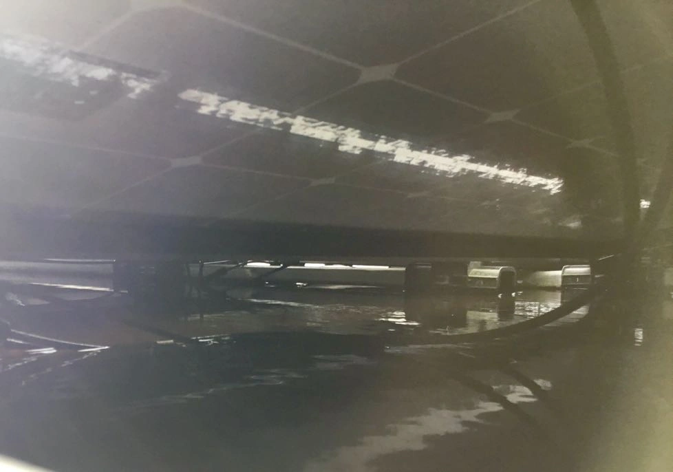 Bottom view of solar panel on flat roof with a layer of water in which cables and connectors hang: this is not how it should be done!