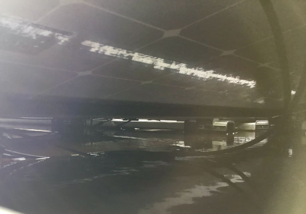 Onderaanzicht van zonnepaneel op plat dak met een laag water waarin kabels en connectoren hangen: zo moet het dus niet!